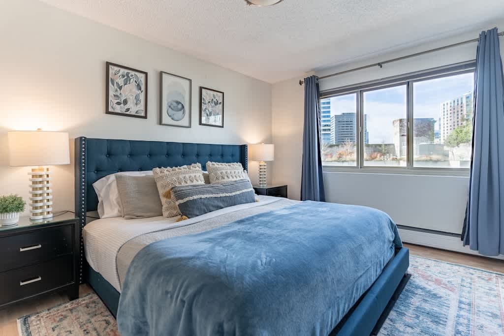 Relax in this serene bedroom with wide windows offering a peaceful glimpse of the city.