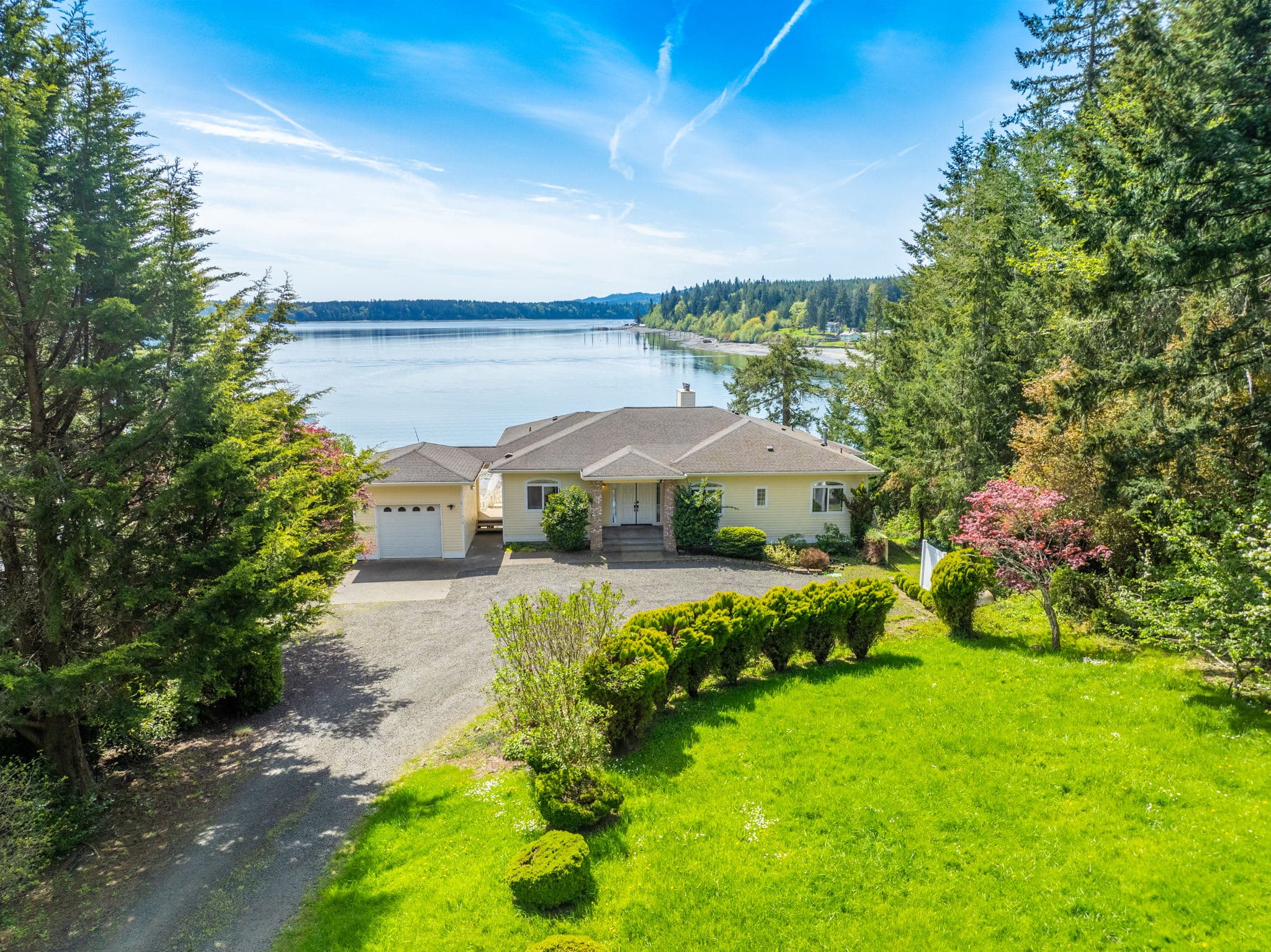 Stunning waterfront home nestled among evergreens with sweeping views, private beach access, and serene privacy at the end of a tree-lined drive.