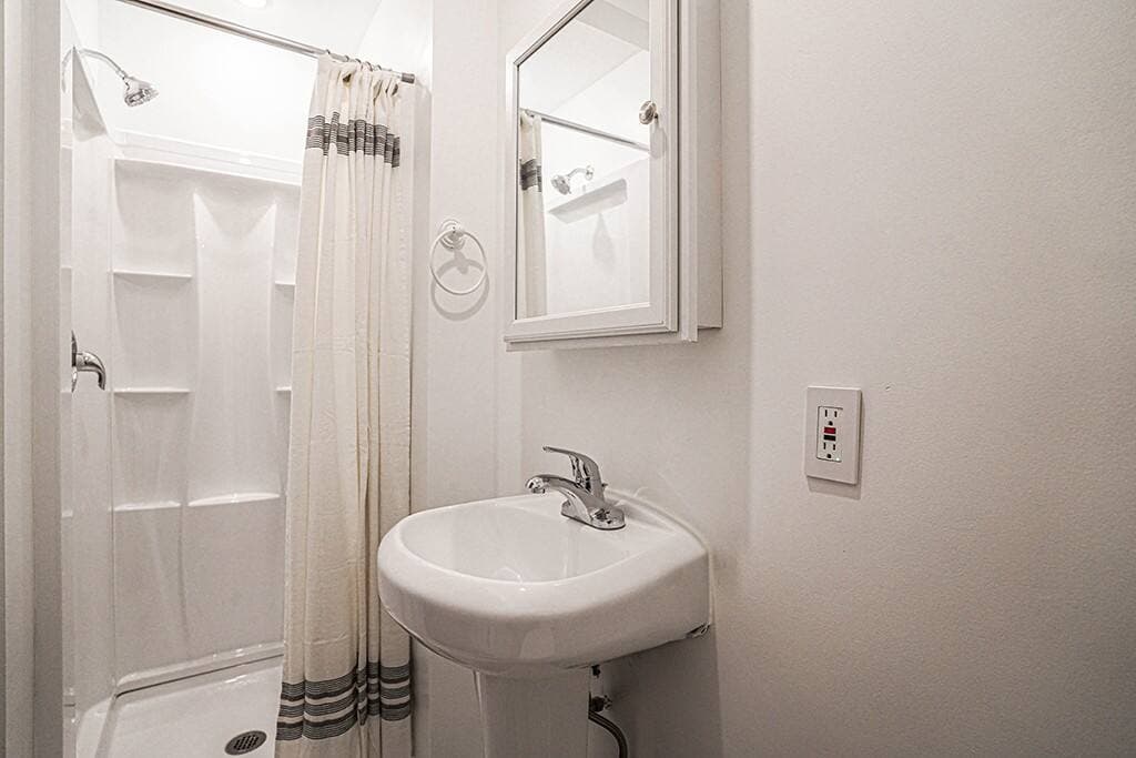 Clean and compact bathroom features a walk-in shower, pedestal sink, and wall-mounted medicine cabinet—offering a functional and efficient layout with a bright, minimalist design.