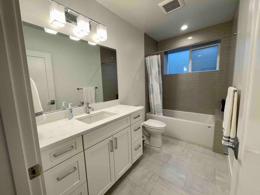 Comfortable bathroom with modern finishes and a clean, streamlined design. Features a full tub, wide vanity, and soft lighting for a relaxing stay.