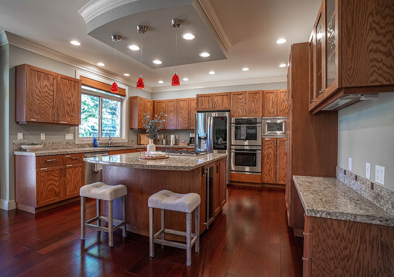 Features warm wood cabinetry, sleek stainless steel appliances including double ovens, a large center island with bar seating, and ample counter space—ideal for cooking, gathering, and entertaining.