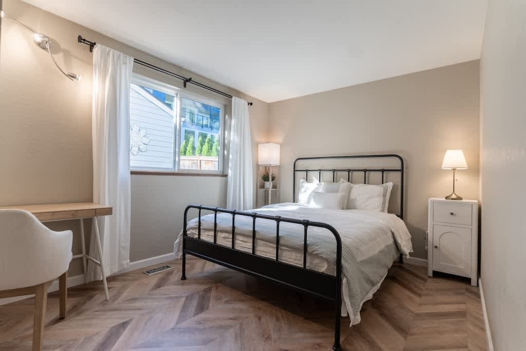 Pristine queen bed in a serene white room, with a cozy desk for productivity.